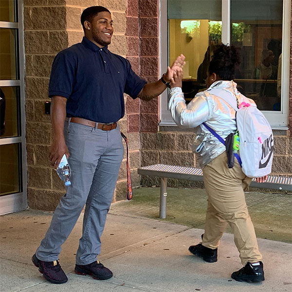 Gabe Smith, Associate Dean of Students, high fiving student outside school