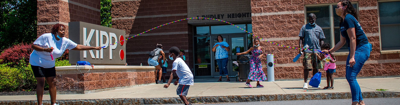 kids and teachers playing jump rope in front of school