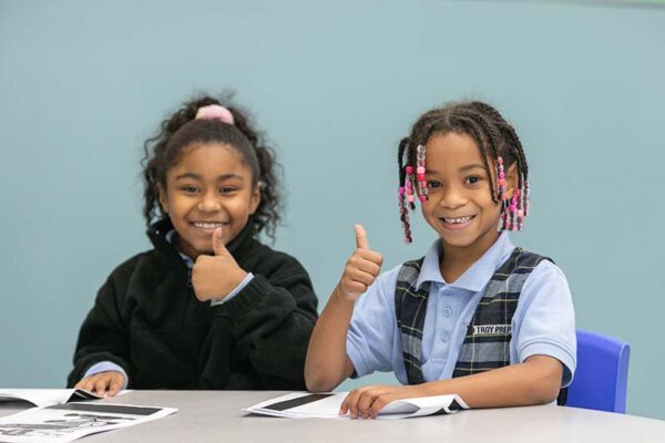 Two little girls smiling at the camera with thumbs up