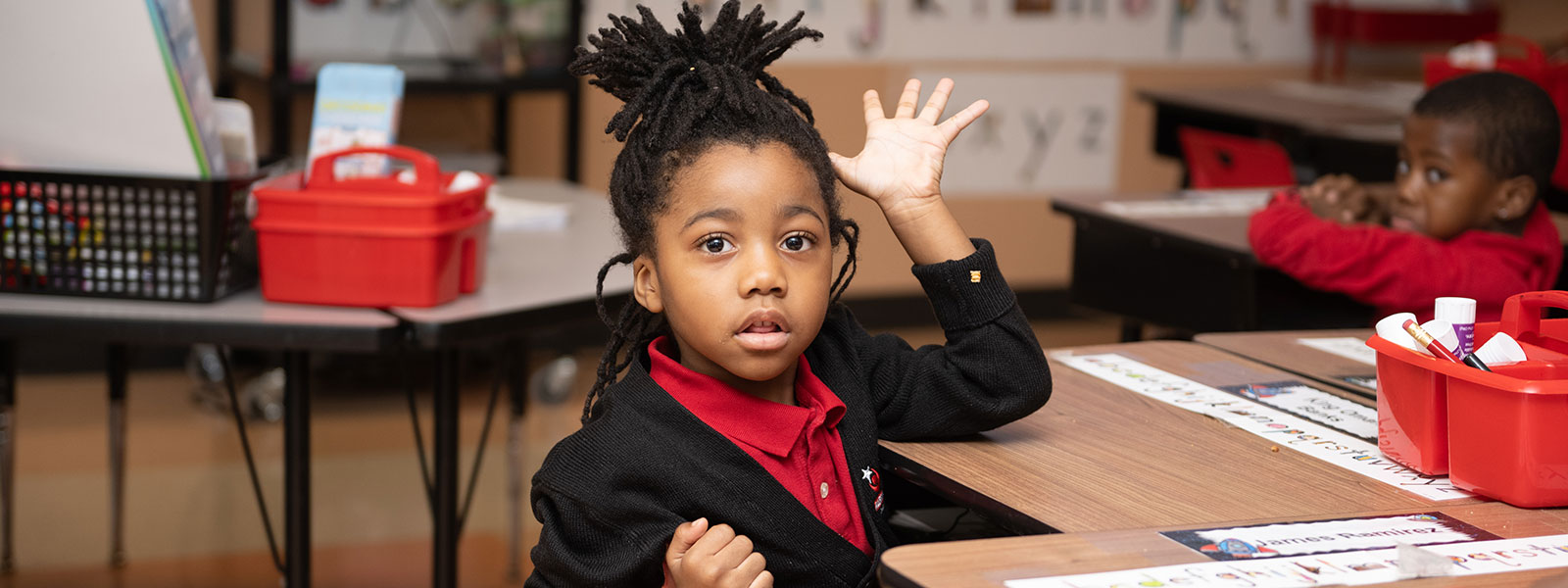 Little girl sitting at a desk raising her hand